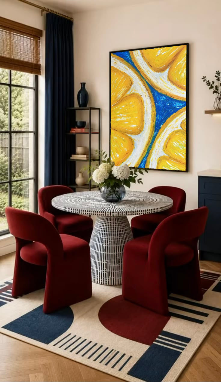 Oversized yellow lemon slices with white rinds against cobalt blue in a black frame on the wall of a dining nook with red chairs